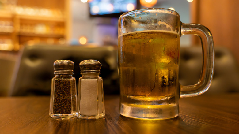 A glass of beer next to salt and pepper shakers