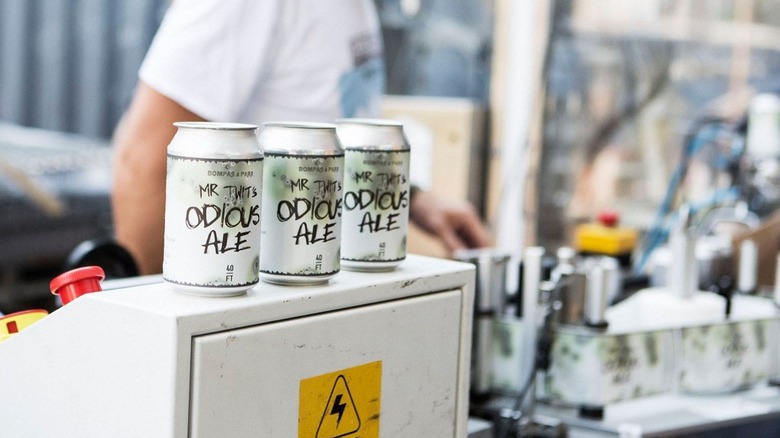 Three cans of Mr. Twit's Odious Ale on top of a control panel with a warning stickerf