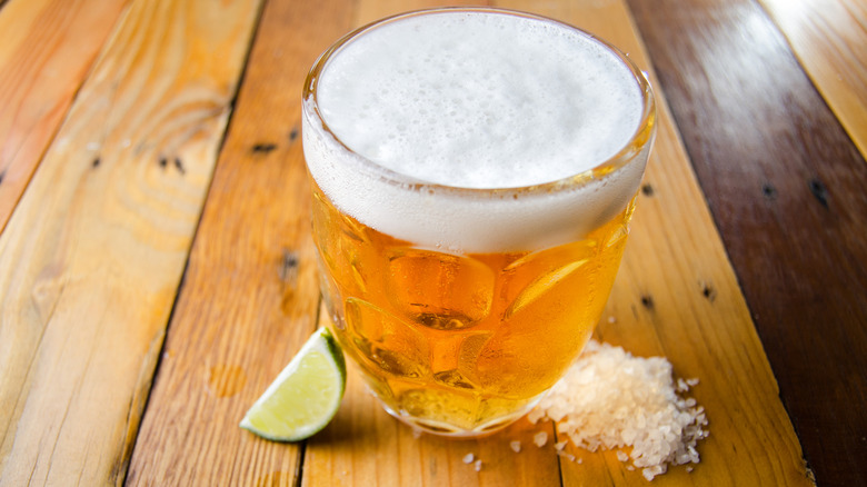 A glass of beer with a pile of salt and a lime