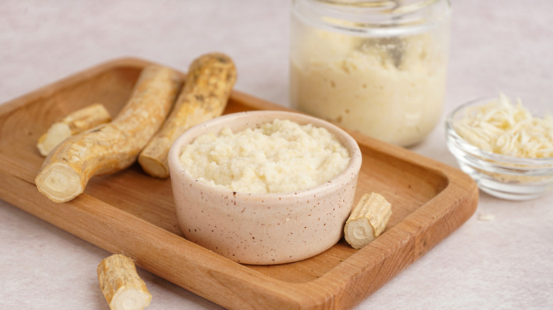 Containers of horseradish sauce with the root on a tray