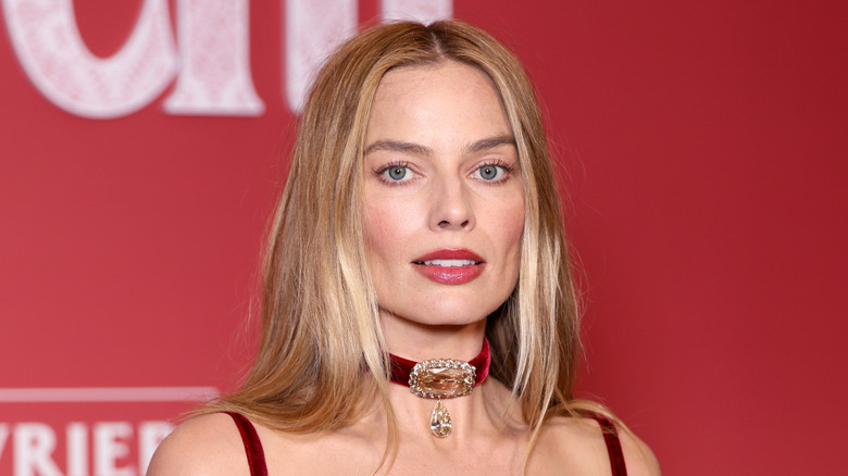 Margot Robbie wearing a jeweled necklace and looking at the camera