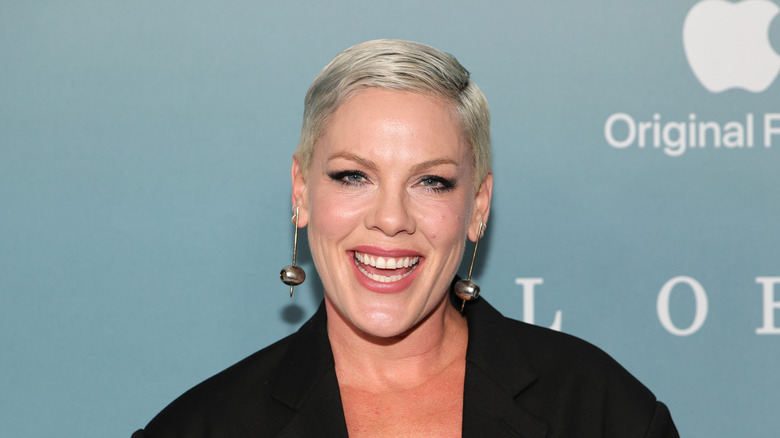Pink wearing bold earrings and a black jacket, smiling