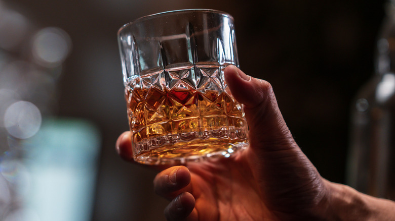 Hand holding a glass of bourbon with blurred background