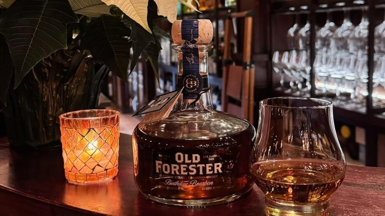 Bottle of Old Forester Birthday Bourbon 2025 with glass on a bar with a candle on the side