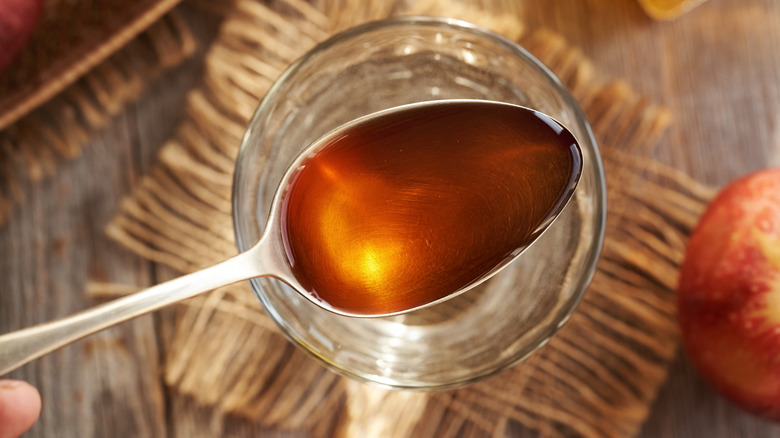 Spoonful of apple cider vinegar held above a table with glass.