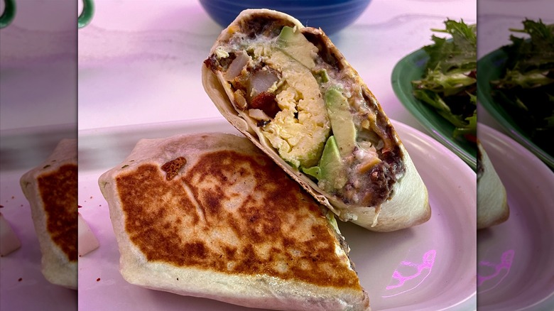 A breakfast burrito cut in half with eggs, home fries, refried beans, and avocado inside