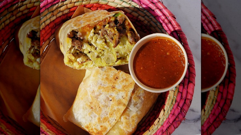 A burrito with carne asada, egg, potato, and cheese in a wicker bowl with chile de arbol salsa on the side