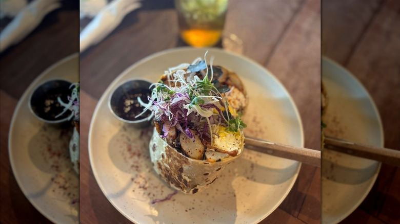 A breakfast burrito on a white plate that's cut in half and has potatoes and eggs in it with micro greens and purple cabbage as a garnish