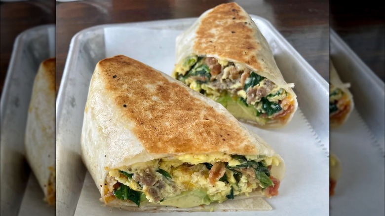 A grilled breakfast burrito cut in half, filled with eggs, sausage, spinach, and avocado on a silver tray