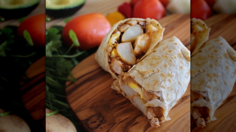 A breakfast burrito cut in half with eggs and potatoes on a wooden board
