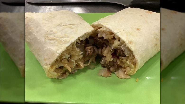 A breakfast burrito cut in half with sausage, hash browns, and melted cheese on a green plate