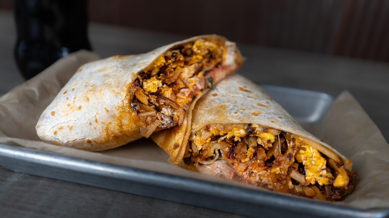 A breakfast burrito cut in half, filled with eggs, hash browns, and cheese served on a tray