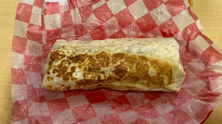 A grilled breakfast burrito on red checkered paper on a table