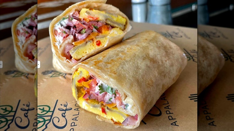 A breakfast burrito cut in half, filled with a garden frittata, sour cream, pico de gallo, and cilantro