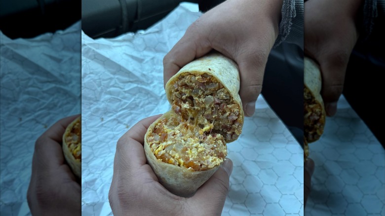 A breakfast burrito cut in half, filled with sausage, bacon, ham, eggs, hash browns, onion, tomato, and cheese
