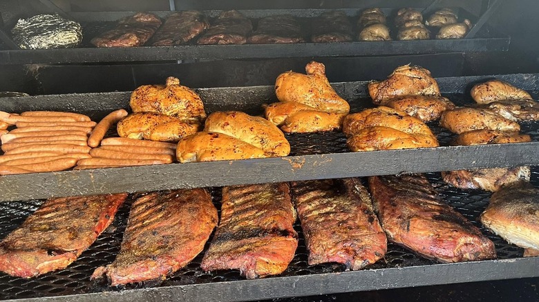 Large smoker with rows of ribs, chicken, hot dogs, and steaks.