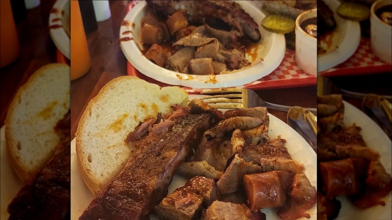 A plate of burnt ends, ribs, and white bread with more barbecue meat in the background.