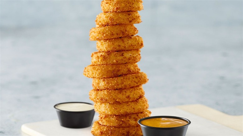 Tall stack of onion rings and two cups of dipping sauces