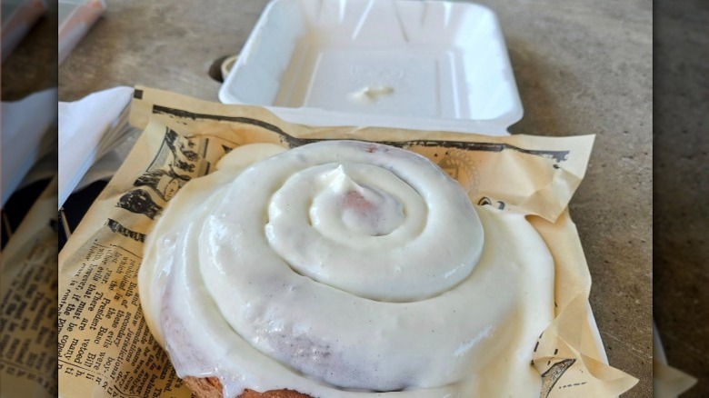 A giant Richter Bakhaus cinnamon roll on newspaper in a styrafoam container