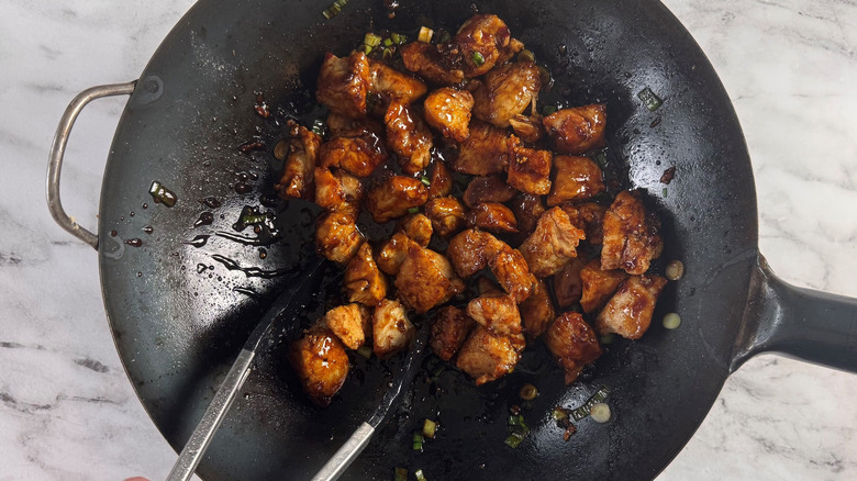 Tongs tossing saucy chicken in wok