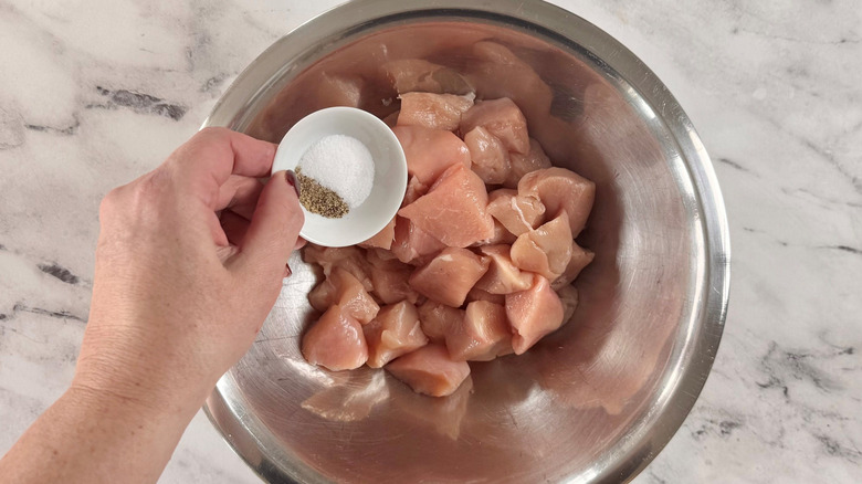 Hand holding bowl of salt and pepper over raw chicken