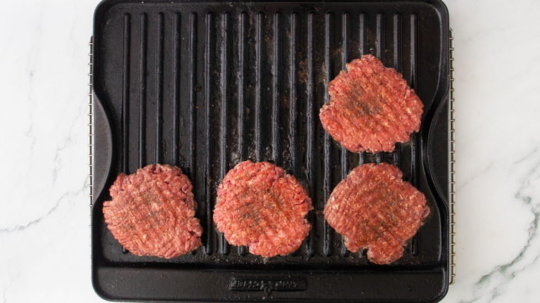 Four seasoned burger patties on grill pan