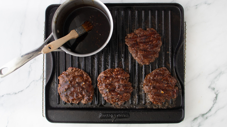 Glazed meat patties and saucepan with teriyaki sauce on grill pan