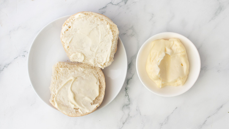 Mayonnaise coated burger buns on plate next to bowl of mayonnaise