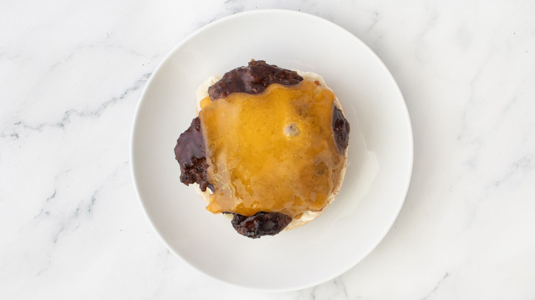 Burger patty with melted cheese sitting on top of a bottom burger bun on a plate