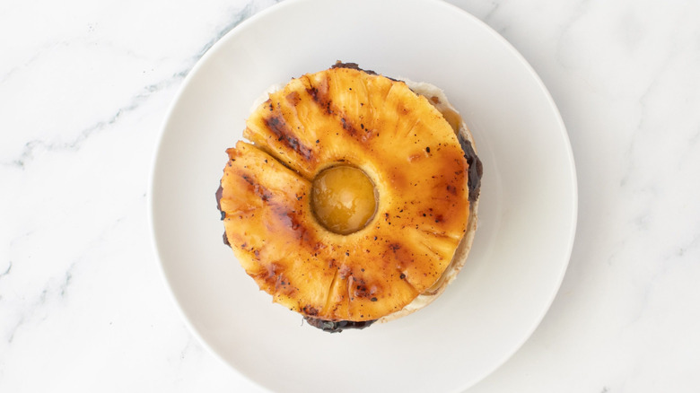 Glazed pineapple ring on top of an opened burger on plate