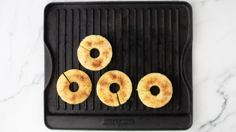 Aerial view of four seasoned pineapple rings on grill pan