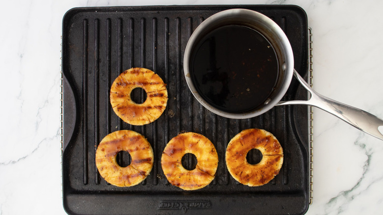 Grilled pineapple rings and saucepan of teriyaki glaze on grill pan