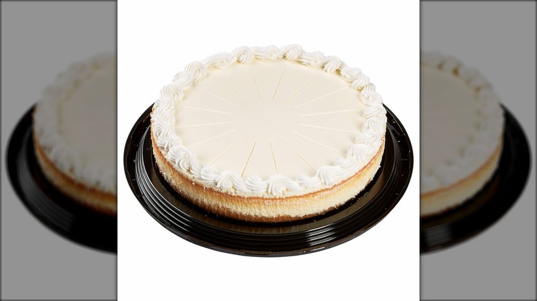 Whole cheesecake with white icing against white background.