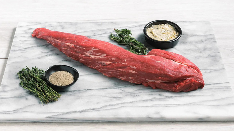 Beef tenderloin on marble cutting board with herbs and spices
