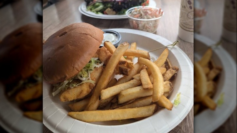 close up of fried haddock sandwich with fries and tartar sauce on paper plate