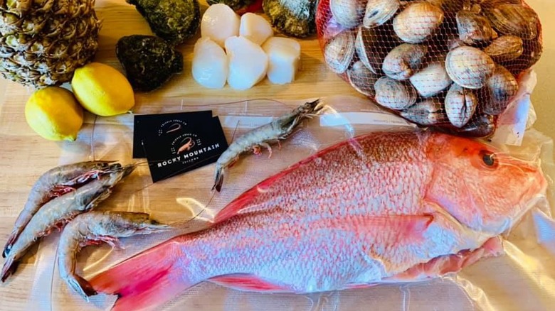 Whole fresh fish and shrimp on cutting board next to clams and rocky mountain seafood business card