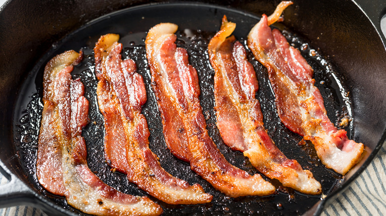 Bacon slices frying in cast-iron pan