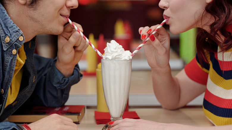 Man and woman in retro diner sharing a milkshake