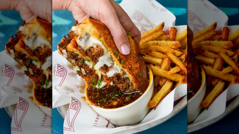 Sandwich being dipped in au jus with fries