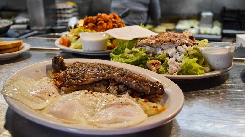 steak and eggs dish with salads in the background