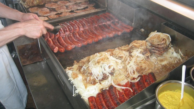 Hamburgers, hot dogs, Polish sausages, and mounds of caramelized onions grilling on a flattop grill