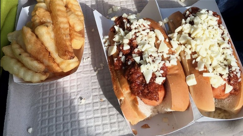 Two hot dogs with chili and cheese and a side of fries on tray.