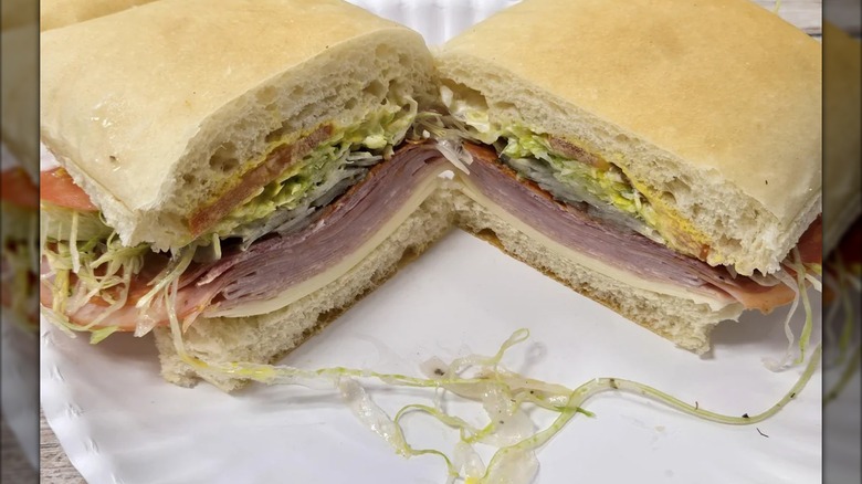 Two halves of an Italian sub with layers of deli meats, provolone, shredded lettuce, and tomatoes