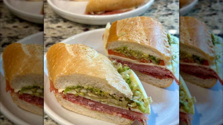 Two halves of an Italian sub on a plate, packed with salami, ham, provolone, shredded lettuce, and a chunky relish-style topping