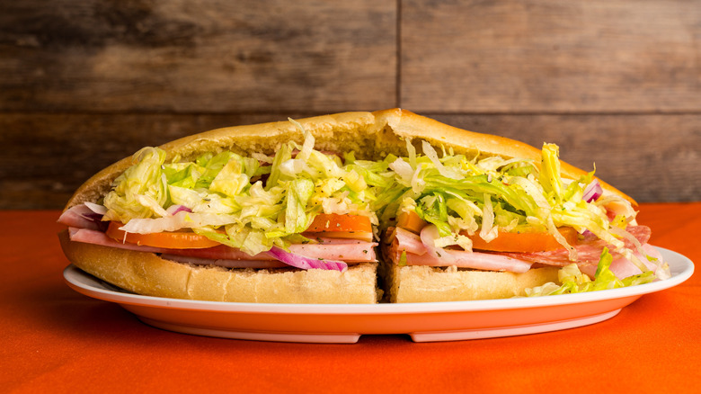 Italian sub sandwich stuffed with deli meats, cheese, lettuce, tomato, and red onion on a white plate