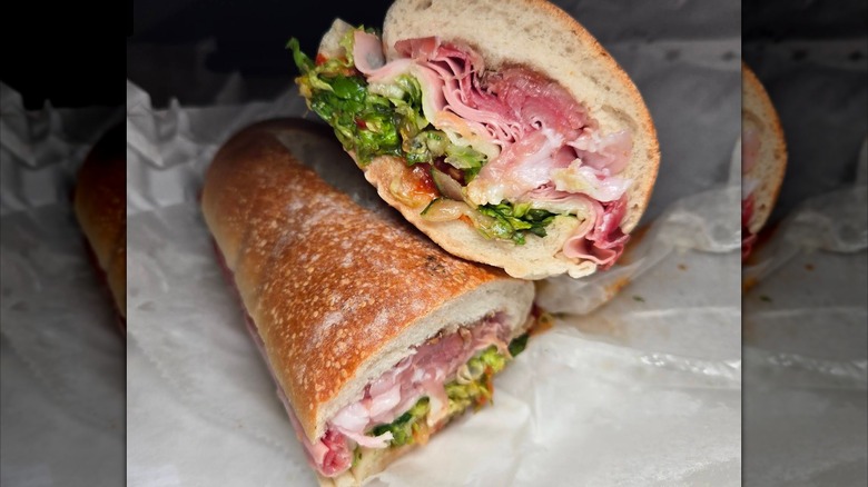 Two halves of an Italian sub on a crusty roll, filled with layers of deli meat and cheese, lettuce, and dressing
