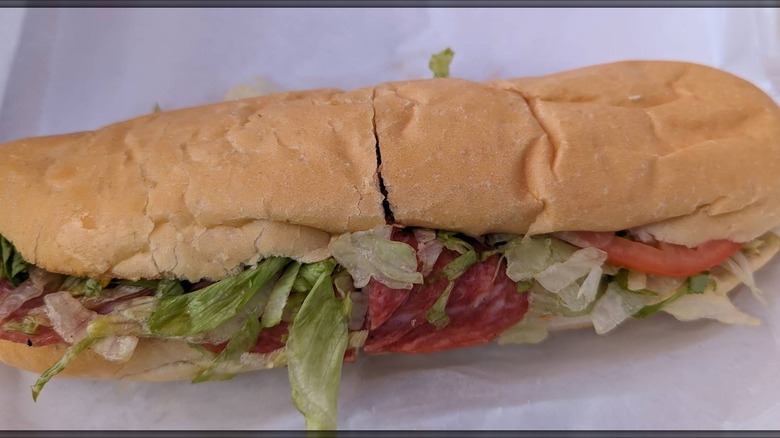 An Italian sub on a soft roll filled with deli meat and cheese, lettuce, and tomato, sliced in half