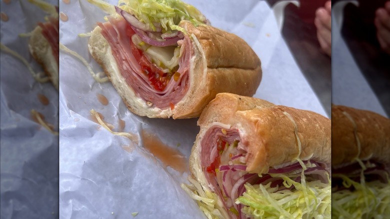 Two cut pieces of an Italian sub on a soft roll, filled with folded deli meats, cheese, lettuce, tomato, and red onion