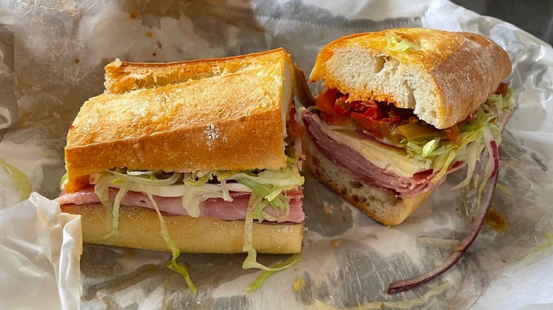 Two halves of an Italian sub on crusty bread, layered with deli meats and cheese, lettuce, red onion, and sweet peppers