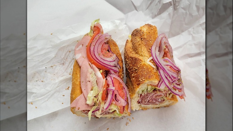 An Italian sub cut into two portions, loaded with deli meats, shredded lettuce, tomato, and slices of red onion